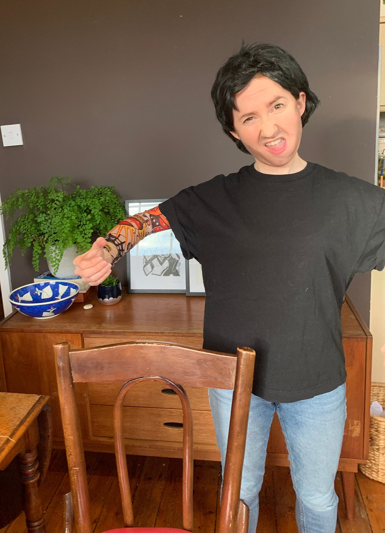 Woman dressed as a man in short black wig and black t shirt making a gross facial expression