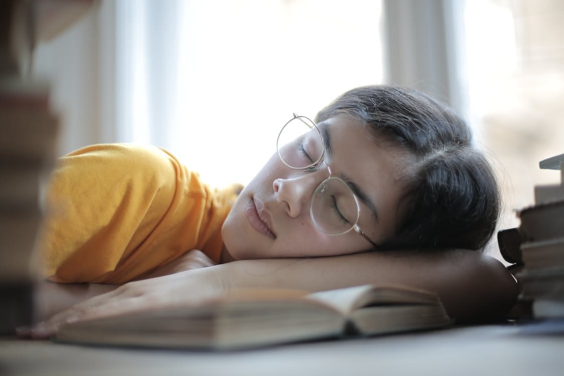 Free Exhausted female student sleeping at table in library Free Exhausted female student sleeping at table in library