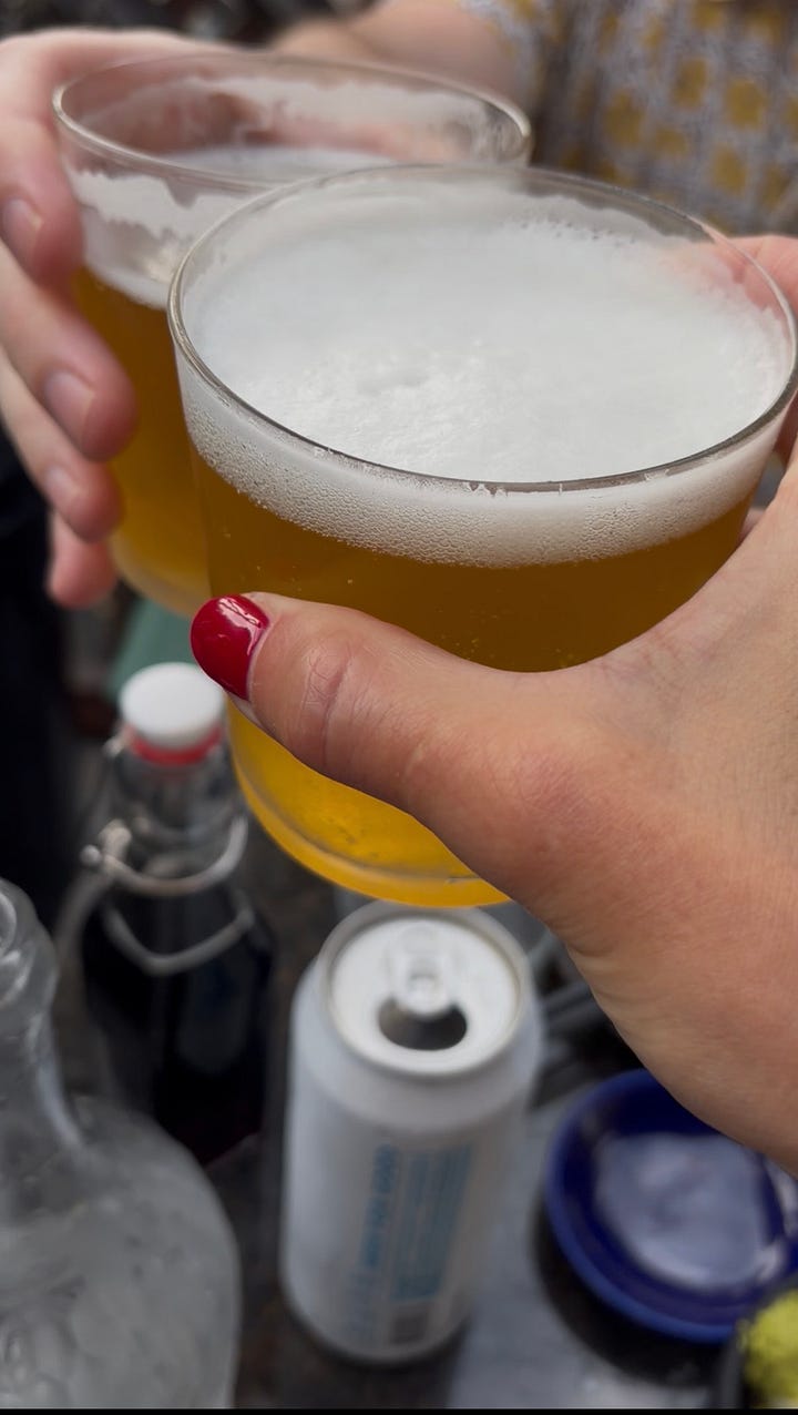 Left: a hand with red nail polish holding a glass of golden IPA with a thick foam head. Right: a close-up of the Patrick the Great roll, crispy sweet potato topped with sesame seeds, avocado, and pickled purple cabbage.