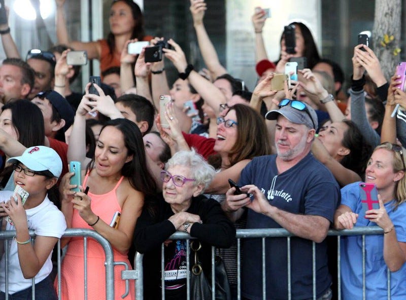 A crowd of people record an event on their phones. A crowd of people record an event on their phones.