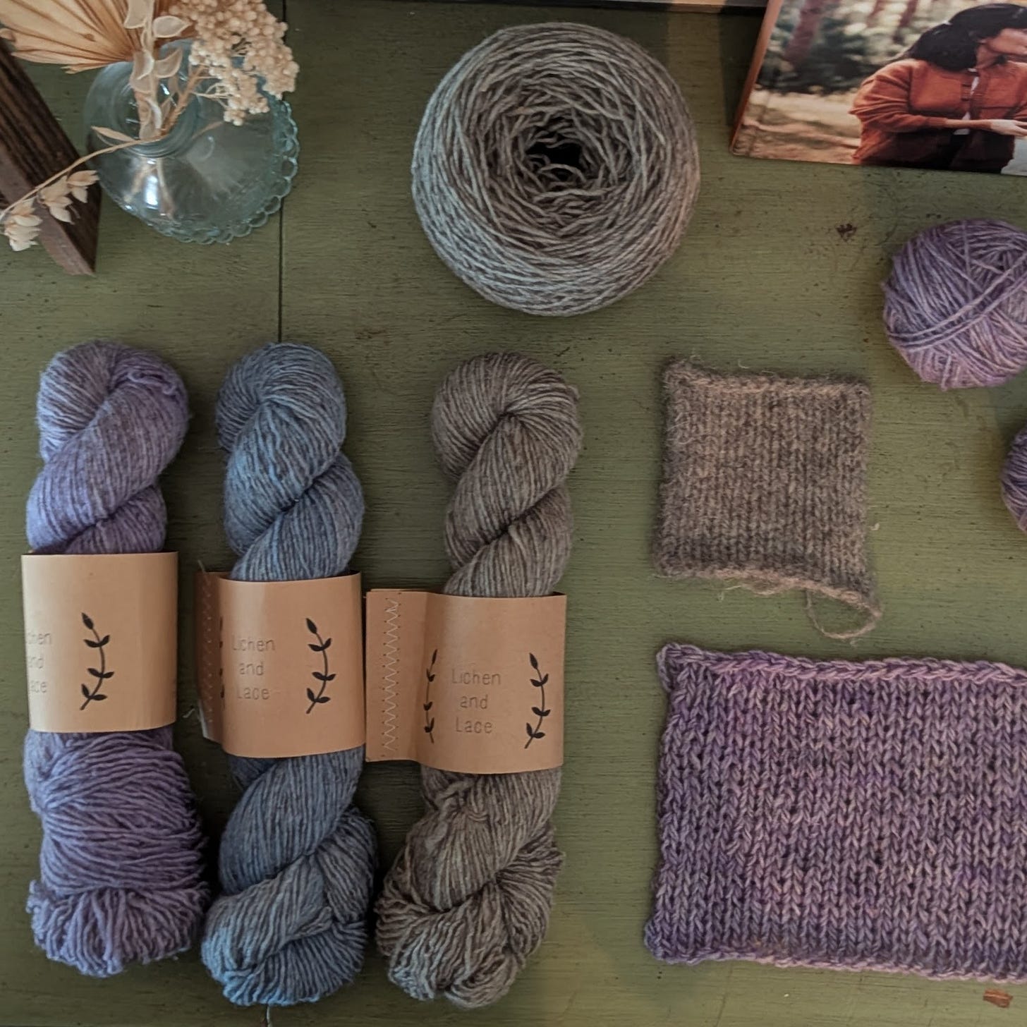 Three skeins of Lichen and Lace in lavender, blue, and sage next two a knit swatch of the lavender yarn and a felted swatch of the sage yarn.