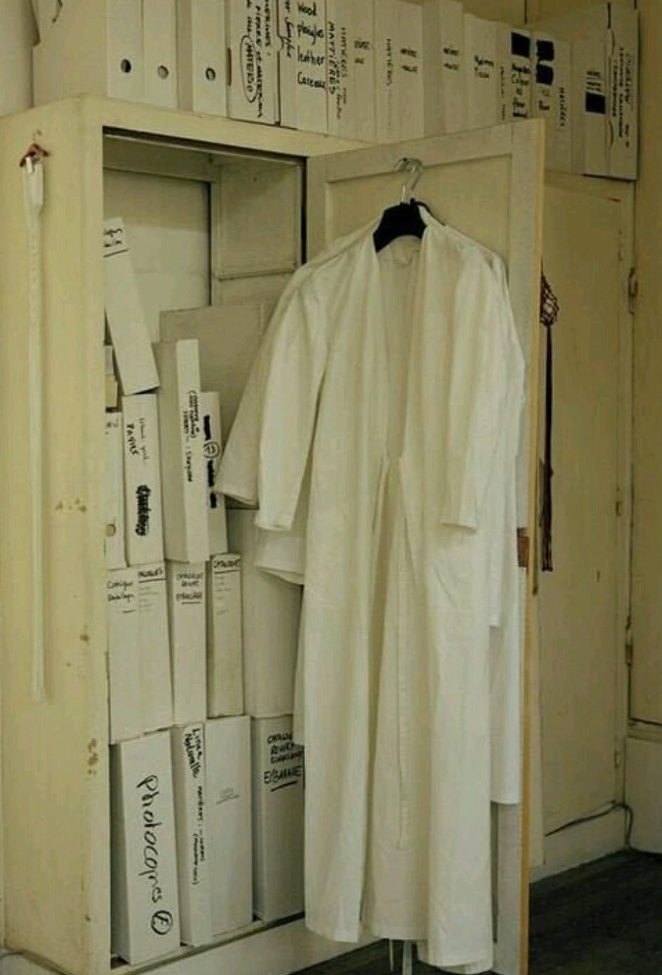 “Photographic and archival imagery of individuals wearing white lab coats as used in the design studio of Maison Martin Margiela. These garments functioned as a symbolic uniform to neutralize hierarchy, promote anonymity, and emphasize collective authorship over individual style. The white coats reflect the psychological and symbolic aspects of enclothed cognition — clothing as a trigger for behavior, identity, and group dynamics.”