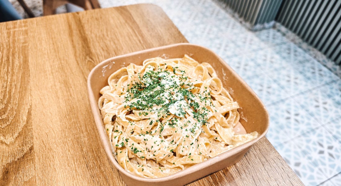 A wooden box with alfredo pasta in it, on top of a wooden table