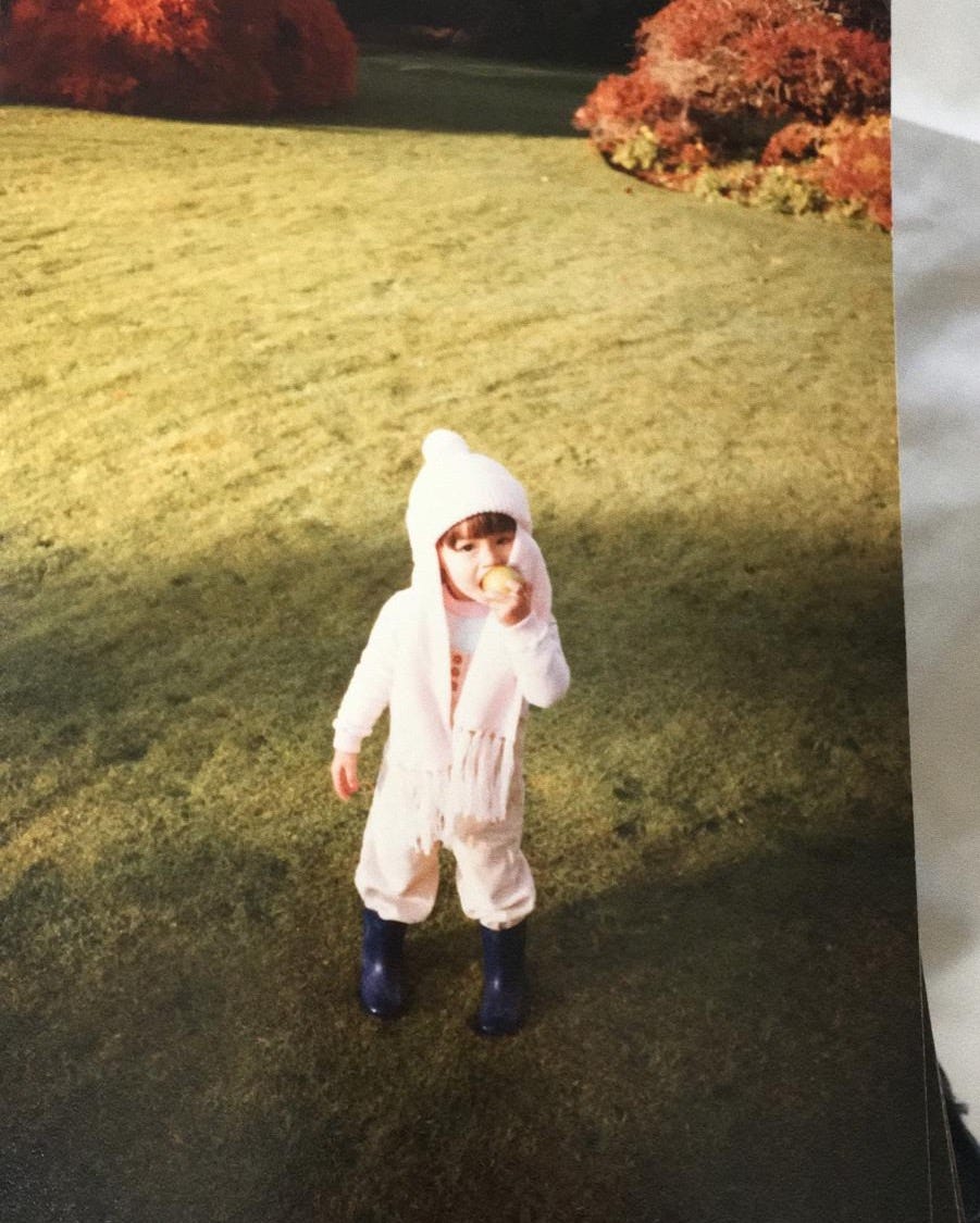 Two year old girl in the 80s eating an apple in garden