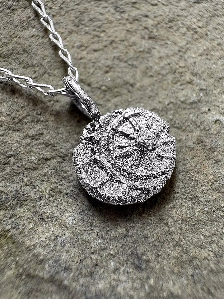 Photo One: a handmade ceramic mug with a medieval cat illustration on one side and the quote, "Bad news for bread, I woke up." on the other.  Second photo: handmade silver pendant of a sun and moon.