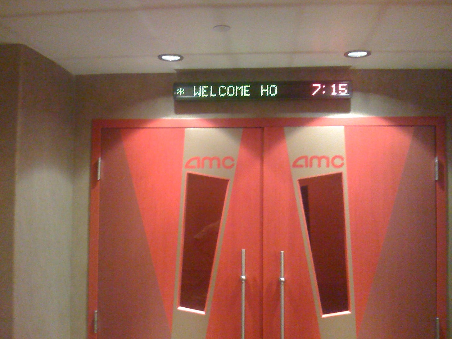 Photo of movie theatre doors. Electronic marquee above the doors read "*WELCOME HO***