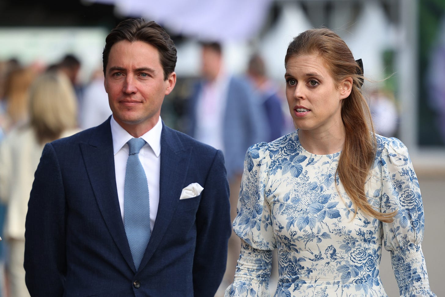 Princess Beatrice in a blue floral dress looking concerned and Edoardo smiling in a navy suit