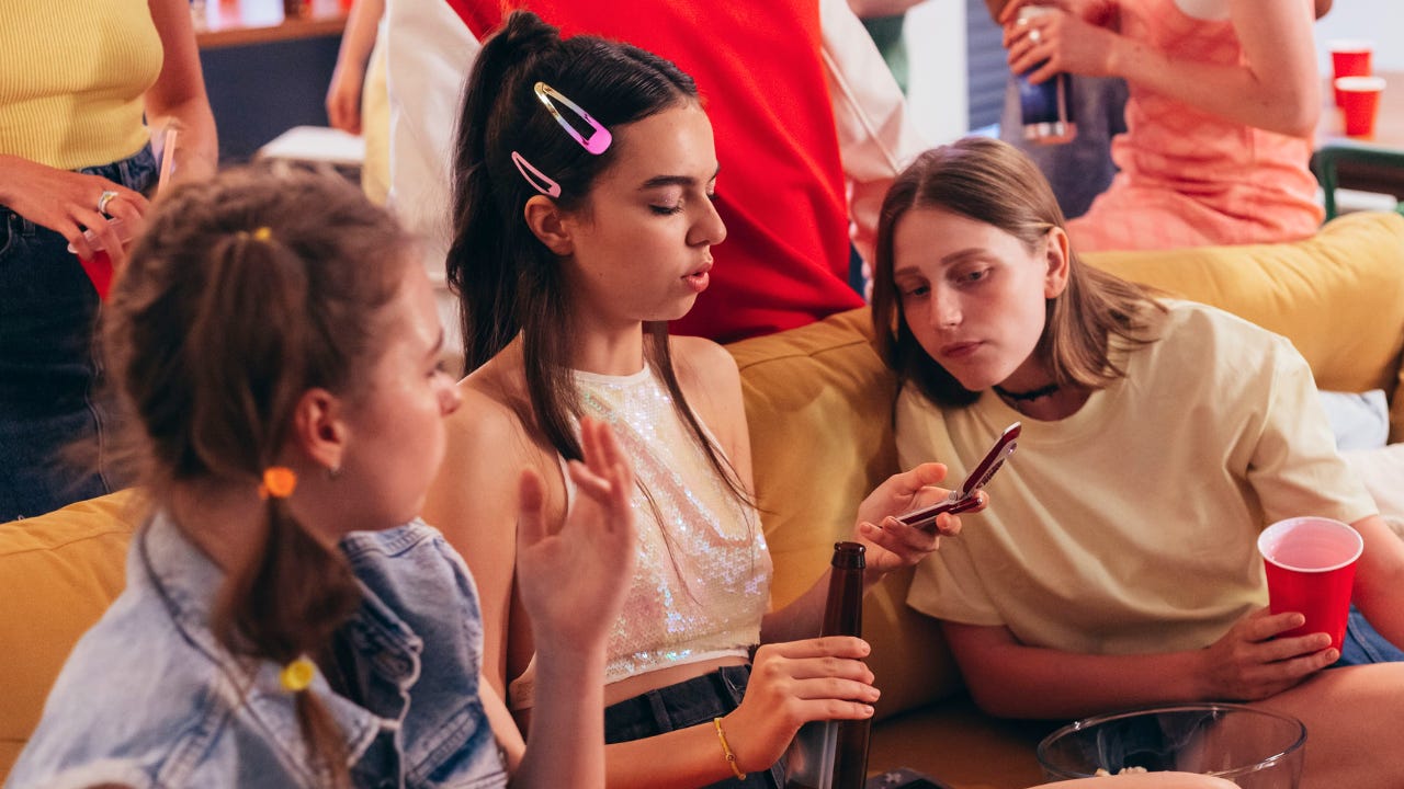 Three teenage girls looking into a flip phone. Three teenage girls looking into a flip phone.