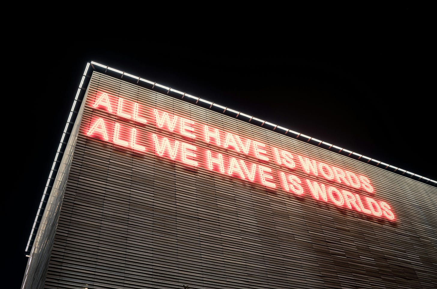 Umwelt - Photo shows a building lit up with the words 'All we have is words - All we have is worlds' flashing in neon lights by the roof. Umwelt - Photo shows a building lit up with the words 'All we have is words - All we have is worlds' flashing in neon lights by the roof.