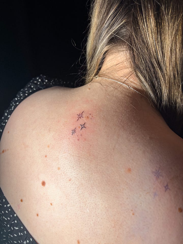 A woman tattoos MG Hunt on her back. The back tattoo is a cluster of 3 stars, in a fine black ink.
