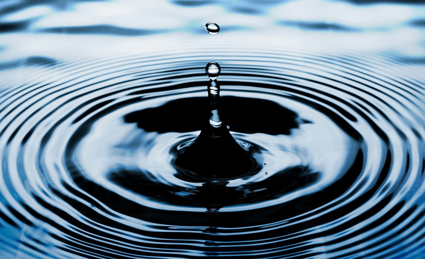 A droplet falling into water and creating a circular ripple effect