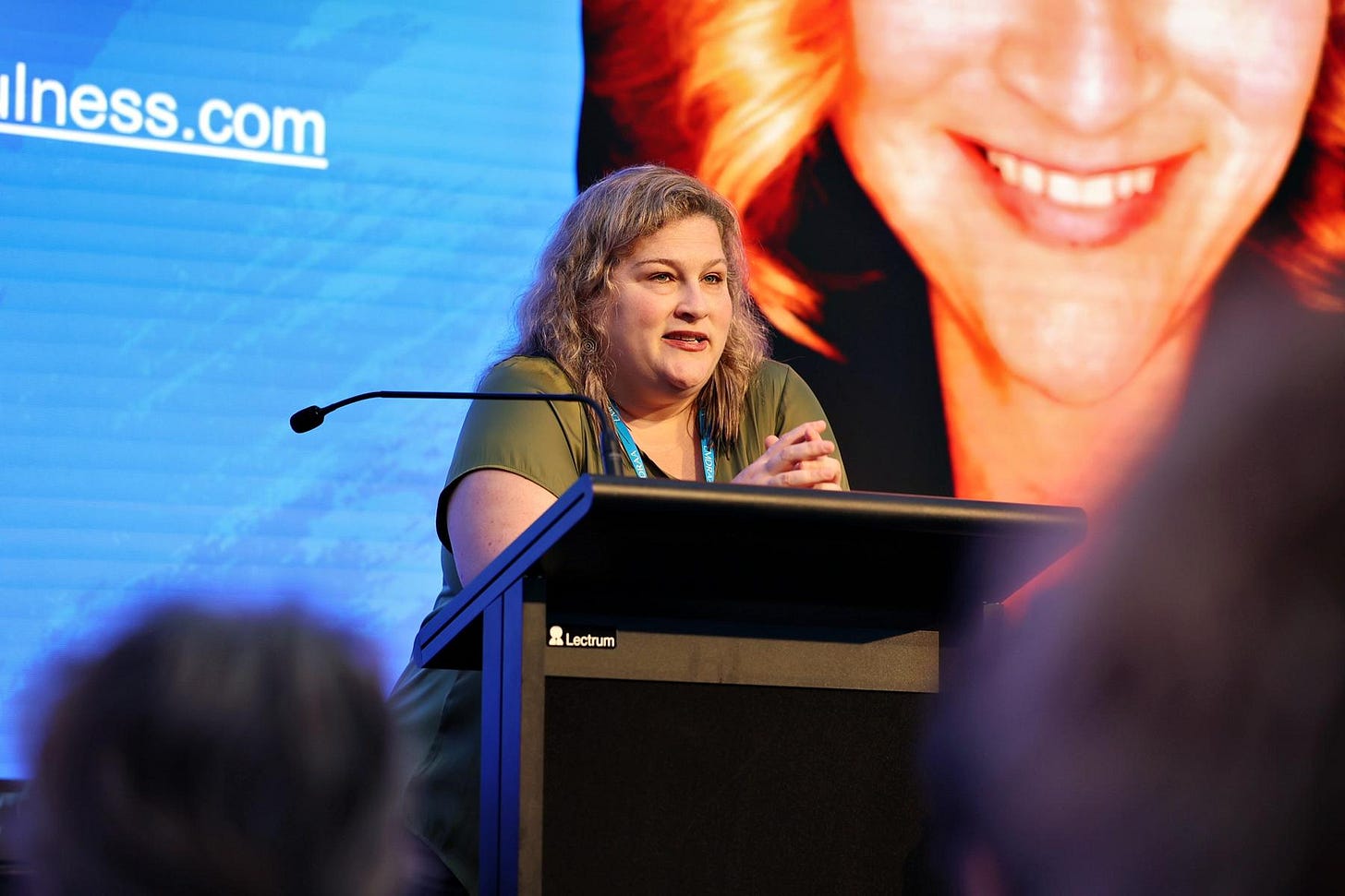 Jamie leaning against a podium in a non-chalant way with a PowerPoint behind her