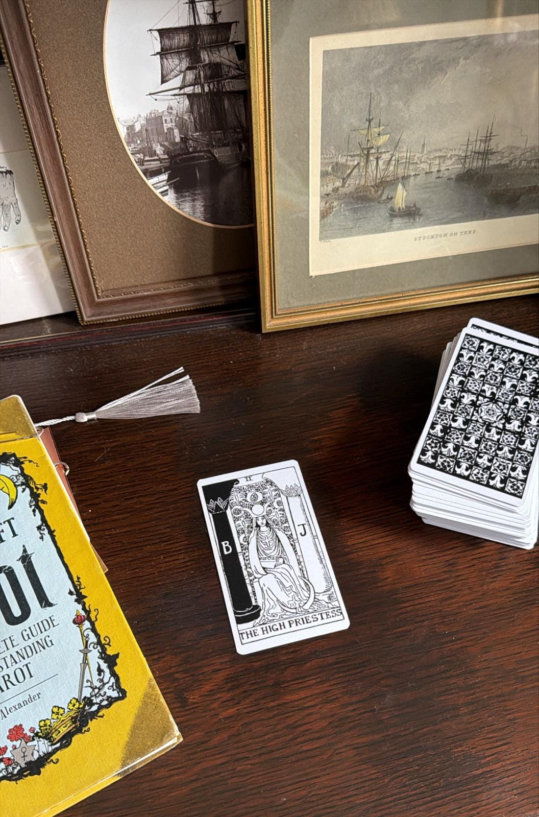 The High Priestess tarot card laid out on a wooden desk beside a tarot guidebook and a stacked deck, photographed during Lucy Rose’s Tarot DMs interview as she draws the final card for a future guest, symbolising intuition, hidden knowledge, and the quiet power of insight that runs through her reflections on creativity and guidance after The Lamb.