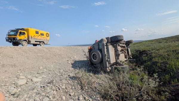 the big yellow truck on the roadway above with a crashed car in the ditch below the big yellow truck on the roadway above with a crashed car in the ditch below