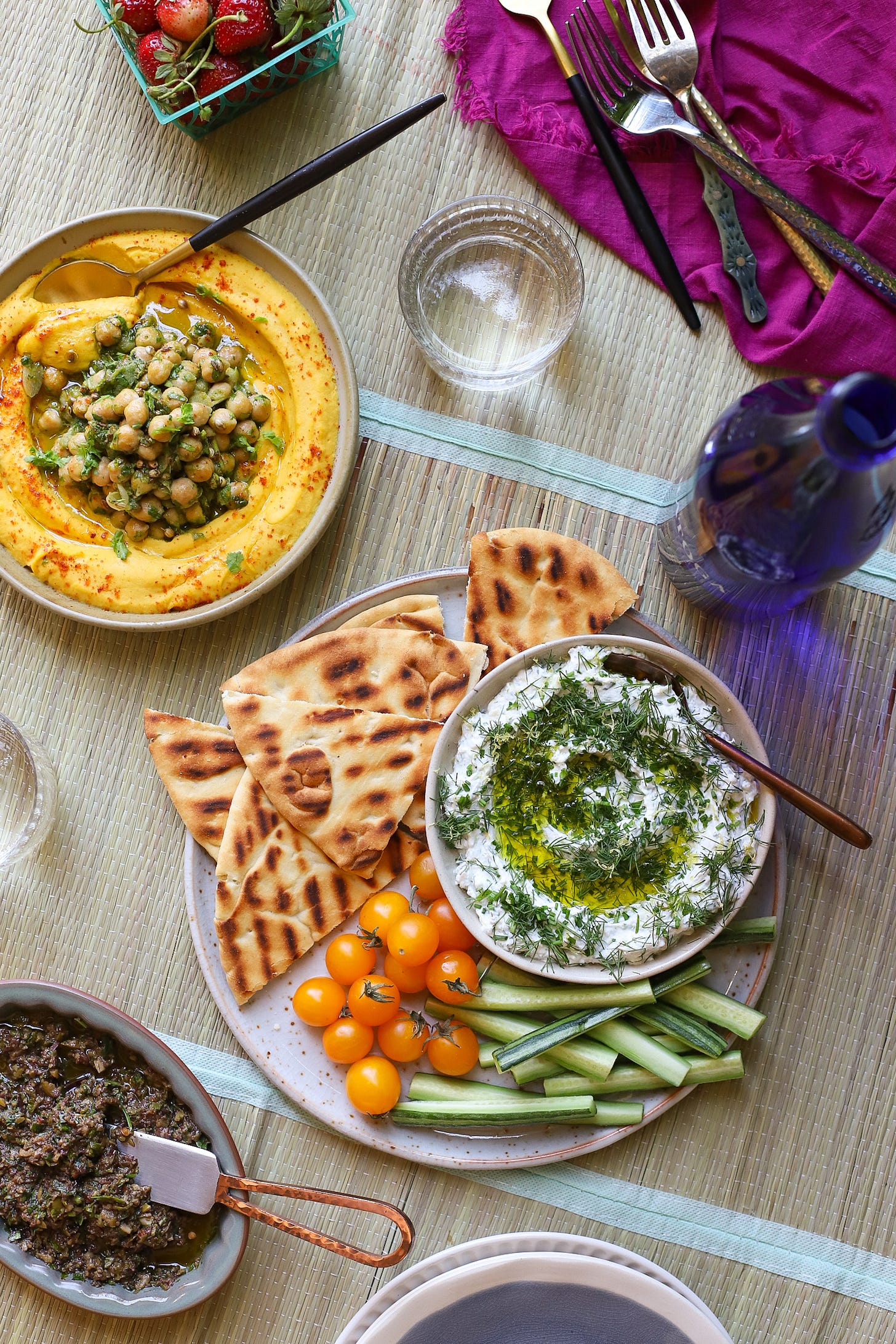 Picnic mat with bowls of carrot hummus, feta-labneh dip, and olive tapenade
