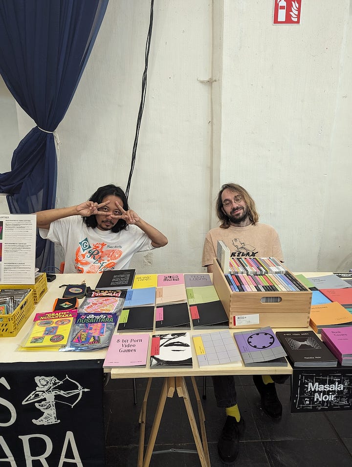 The first image is a poster for the Ghent Art Book Fair, held at Kunsthal Gent on May 11-12, 2024. The poster features bold black text with abstract design elements and lists various participating exhibitors and collaborators, such as Athena! Clay Fair, Imposed Alphabet, and Kero Zine. The second image shows an indoor art book fair scene with high ceilings and colorful tapestries on the walls, featuring multiple booths and tables where people browse through a variety of art books. The space has a grand, church-like architectural style with large windows, wooden beams, and hanging sculptures. In the third image, a person stands behind a booth at the Ghent Art Book Fair, displaying several art books and sticker packs, with a sign indicating that a free sticker pack comes with every book. The table includes works from Soi Books, with a variety of zines, books, and promotional items laid out. The fourth image captures two booth operators from the publishing house Grafis Nusantara sitting behind a table that displays various colorful books, zines, and art publications. One of them is making a peace sign while the other is smiling casually, creating a laid-back and friendly atmosphere at the event.