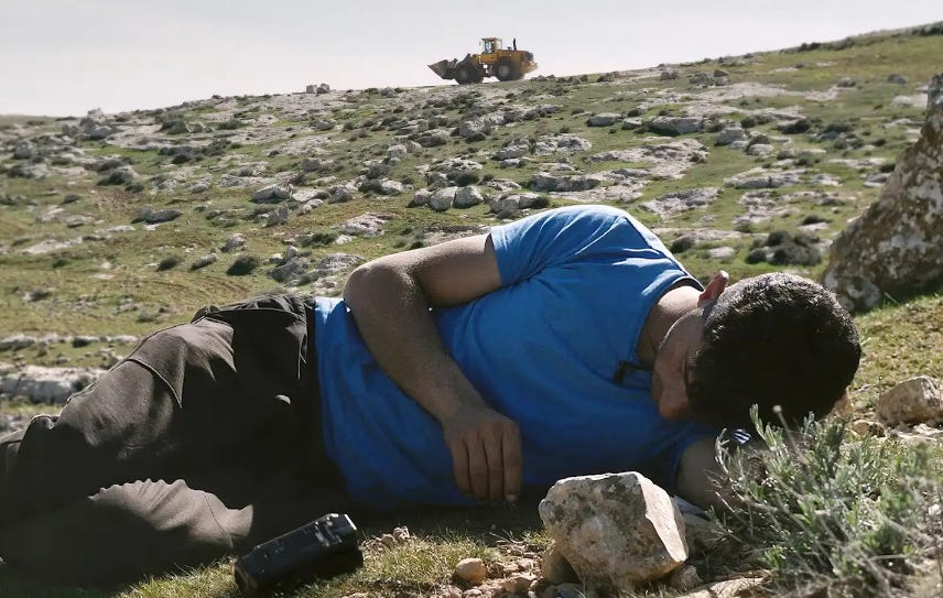 a Palestinian man lies on the ground while a front end loader drives in the background a Palestinian man lies on the ground while a front end loader drives in the background