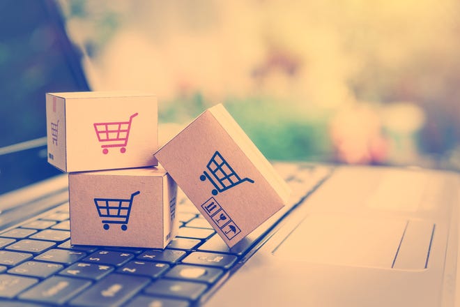 A photo of a laptop with three small cardboard packages stacked on the keyboard with shopping cart icons printed on each side of the box.