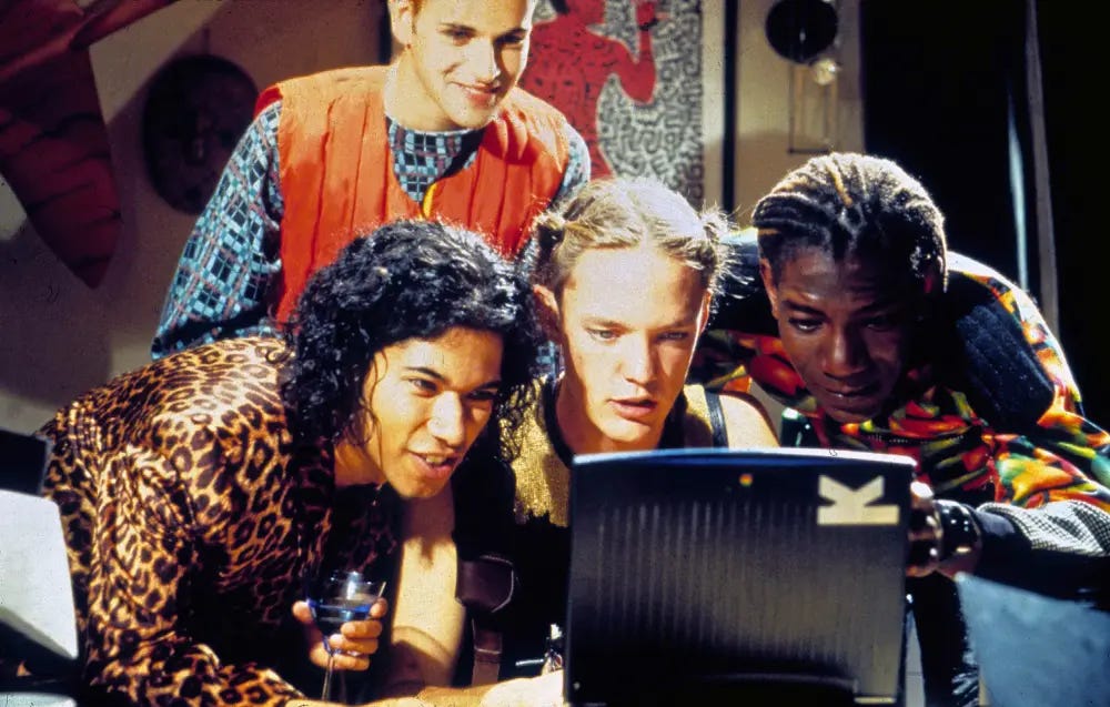 a still image from the movie Hackers of four people crowding around a laptop