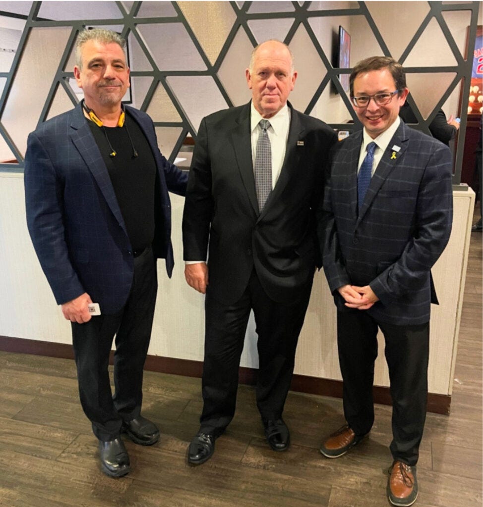 Three people dressed in dark suits standing in front a wall with geometric designs. Three people dressed in dark suits standing in front a wall with geometric designs.