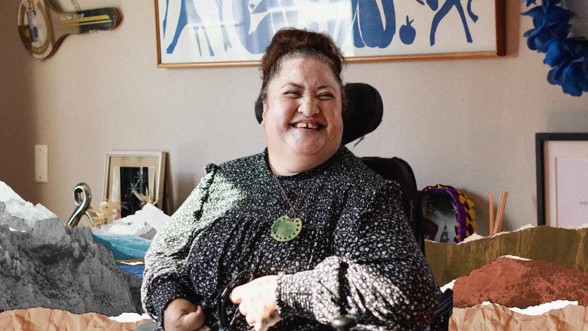Lusi sits in her decorated living room. She is smiling to the side, and wears a black floral blouse and pounamu necklace.