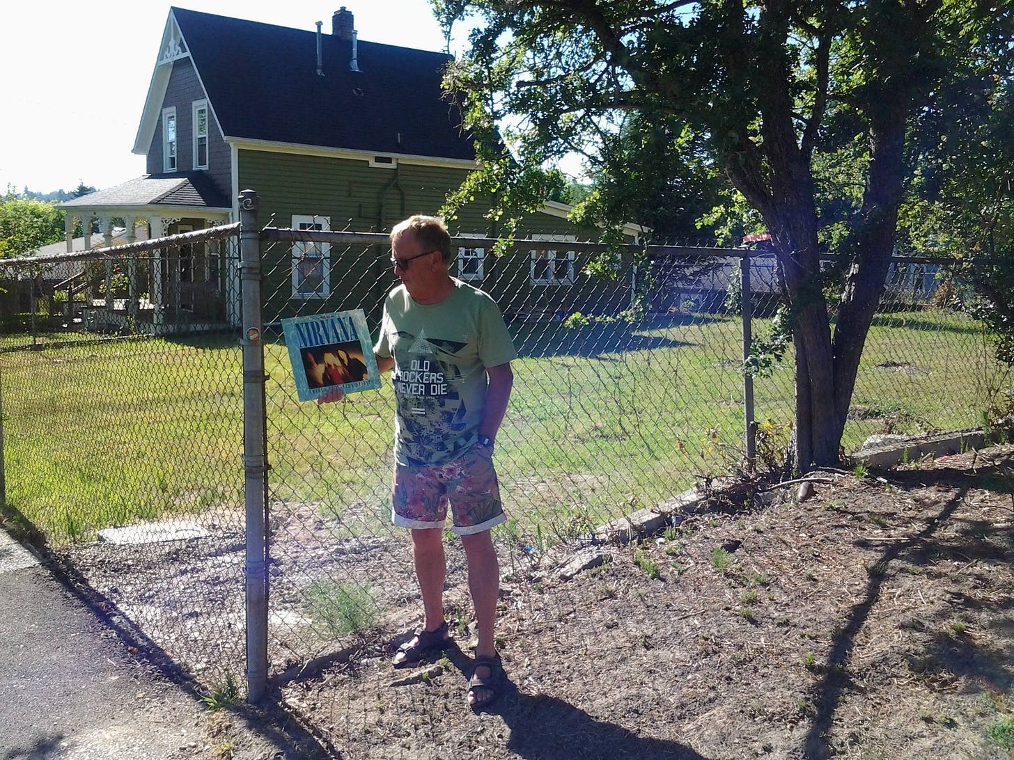 A man standing in front of Kurt Cobain's house with an EP in hand. A man standing in front of Kurt Cobain's house with an EP in hand.