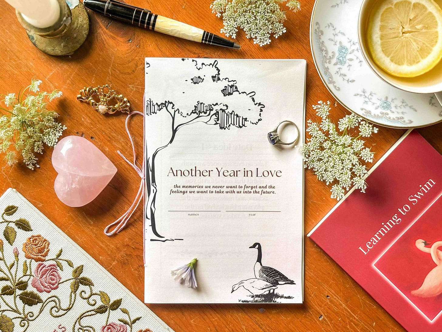 Another Year in Love couples journal flat lay with tea, flowers, rose quartz crystal, and vintage styling - relationship time capsule journal for preserving love story memories