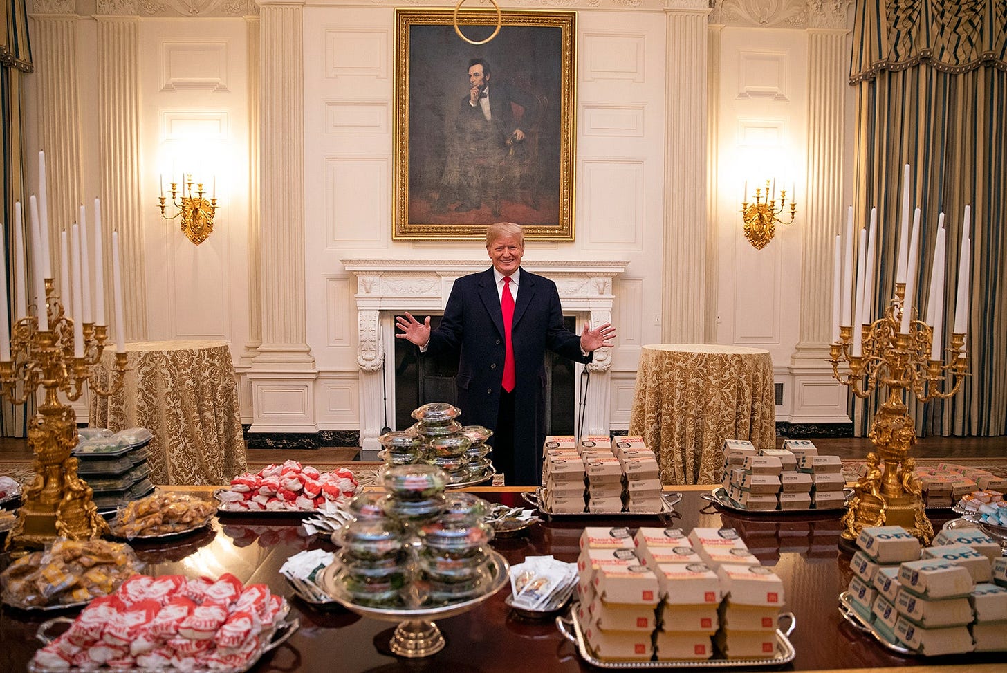 Donald Trump stands behind a table of fast food.