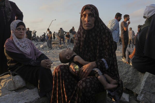 Somoud Wahdan looks at the camera as she sits with her child in an area in the northern Gaza Strip, while waiting for trucks with humanitarian aid to arrive, in Gaza City, Friday, July 25, 2025. (AP Photo/Abdel Kareem Hana)