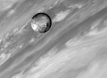 Io, one of Jupiter's moons, against the backdrop of Jupiter's swirling clouds. The image is in black and white, highlighting the contrast between Io's detailed, cratered surface and the smooth, dynamic cloud patterns of Jupiter. Io, one of Jupiter's moons, against the backdrop of Jupiter's swirling clouds. The image is in black and white, highlighting the contrast between Io's detailed, cratered surface and the smooth, dynamic cloud patterns of Jupiter.