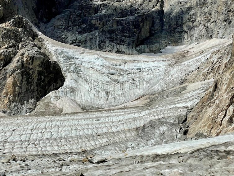 Four people look tiny from a distance as they walk across a vast glacier