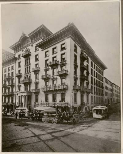 Historic European corner building with ornate architecture, balconies, and period vehicles on street.