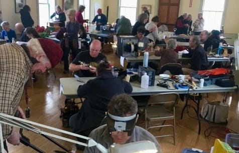 People at tables repairing household items.