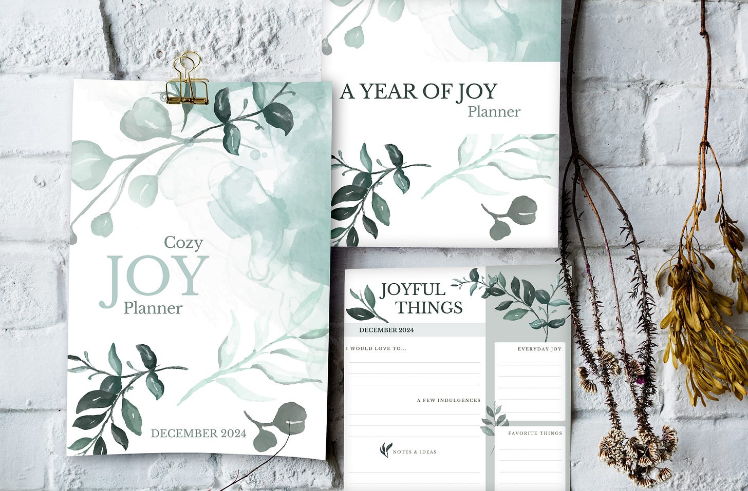Three pages of the Joy planner hanging on a white brick wall, surrounded by pretty dry twigs Three pages of the Joy planner hanging on a white brick wall, surrounded by pretty dry twigs