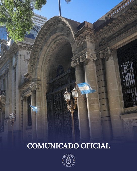 A building with an arched entrance, stone columns, and ornate architectural details. Argentine flags are visible, fluttering near the entrance. Street lamps stand in front of the building. The text "COMUNICADO OFICIAL" and a seal are overlaid at the bottom.