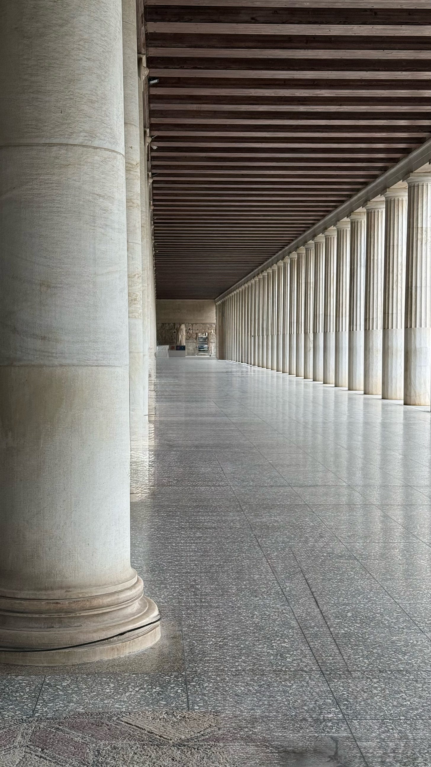 Long colonnade corridor with repeating classical columns receding to vanishing point, shot from floor level showing textured marble floor in foreground