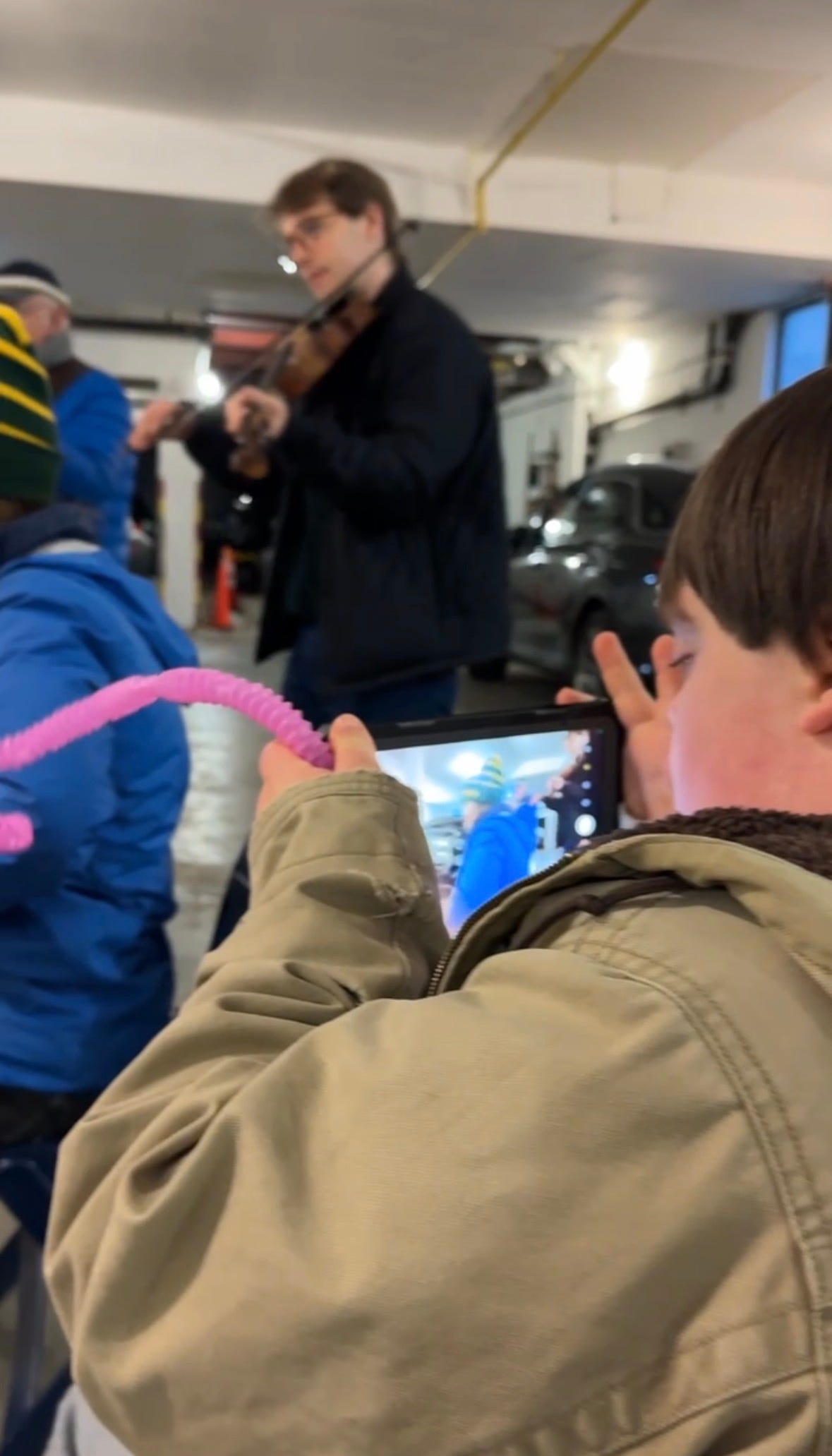 a young man holds up an IPad, recording musicians. A man stands playing a violin. a young man holds up an IPad, recording musicians. A man stands playing a violin.