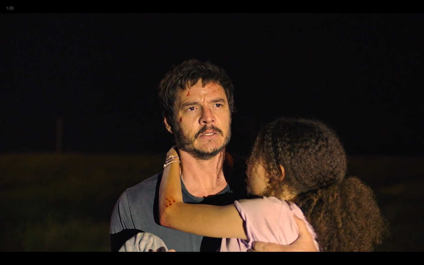A screencap from HBO's The Last of Us, episode 1. Joel is holding Sarah in his arms and looking off to the right side of the screen while a bright light shines onto them both.