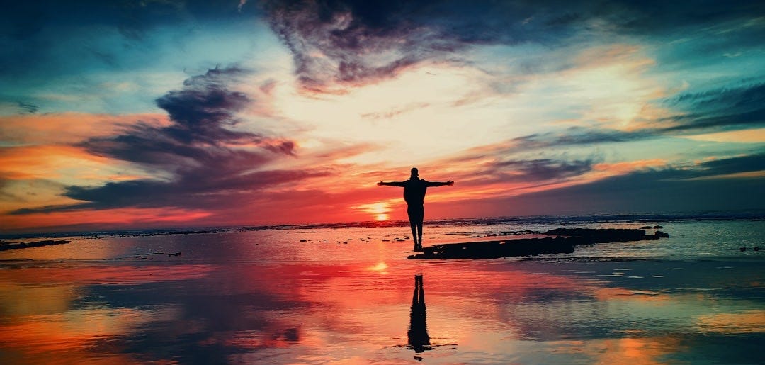 silhouette of person standing on rock surrounded by body of water