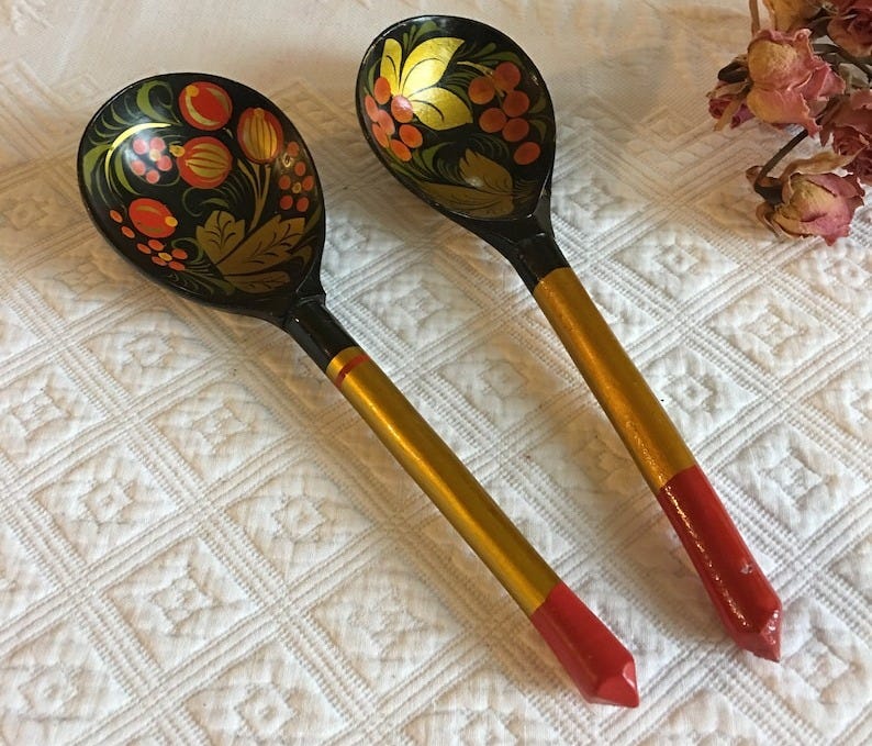 May include: Two wooden spoons with black painted bowls and gold handles. The bowls are decorated with red, orange, and yellow flowers and berries. The handles are painted gold with red tips.