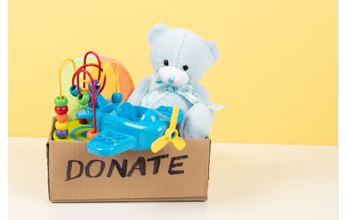 Cardboard box labeled "donation" filled with an interactive game, airplane, ball, and teddy bear.
