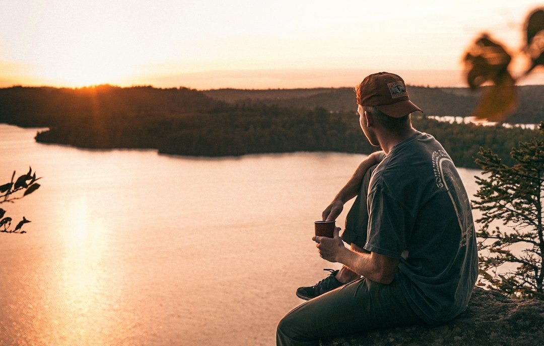 a man sitting on top of a rock next to a body of water