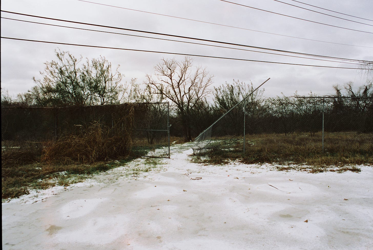 Broken fence at edge of empty lot in snow