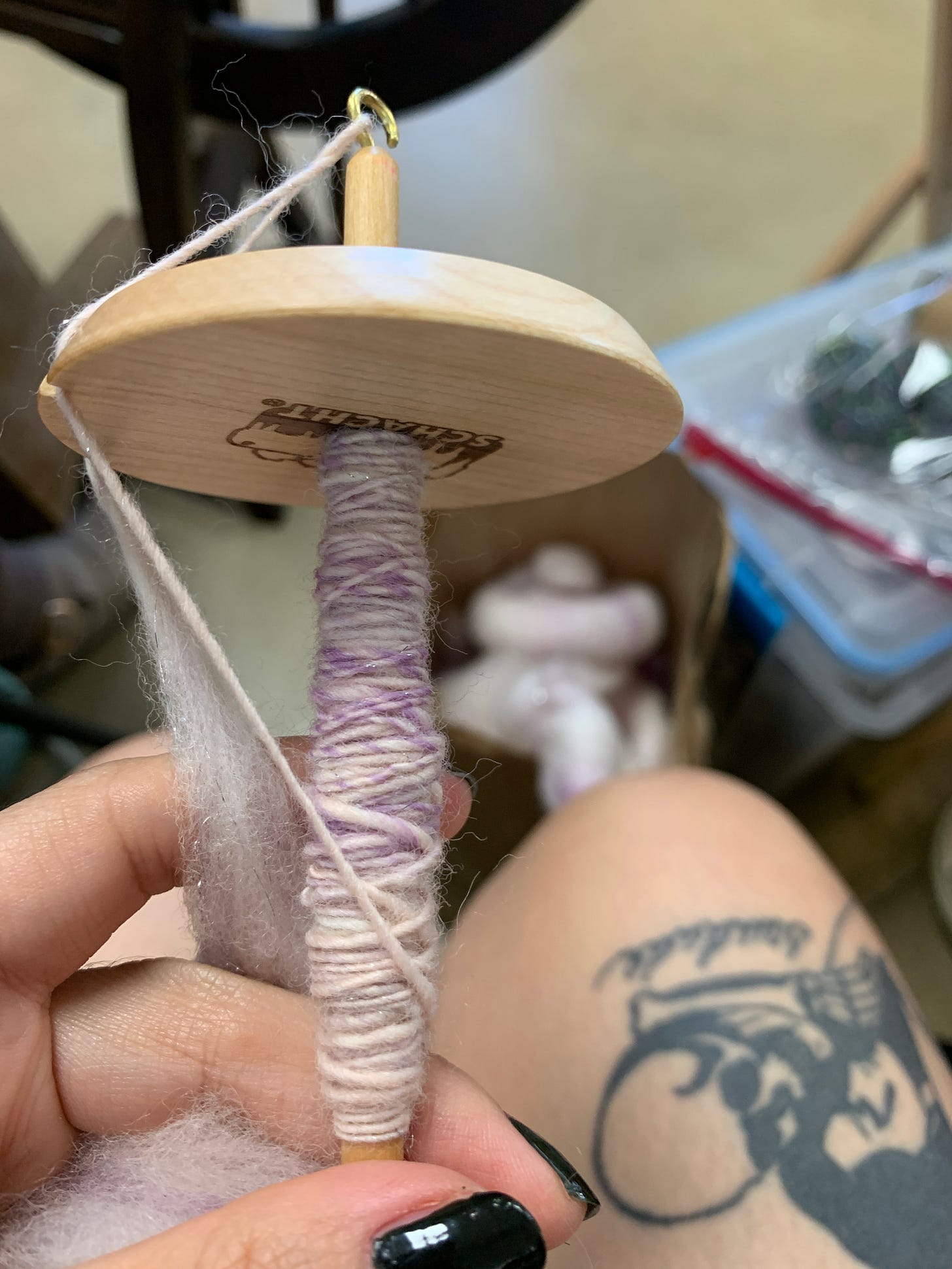 A wooden drop spindle with custom pink, purple, and white yarn