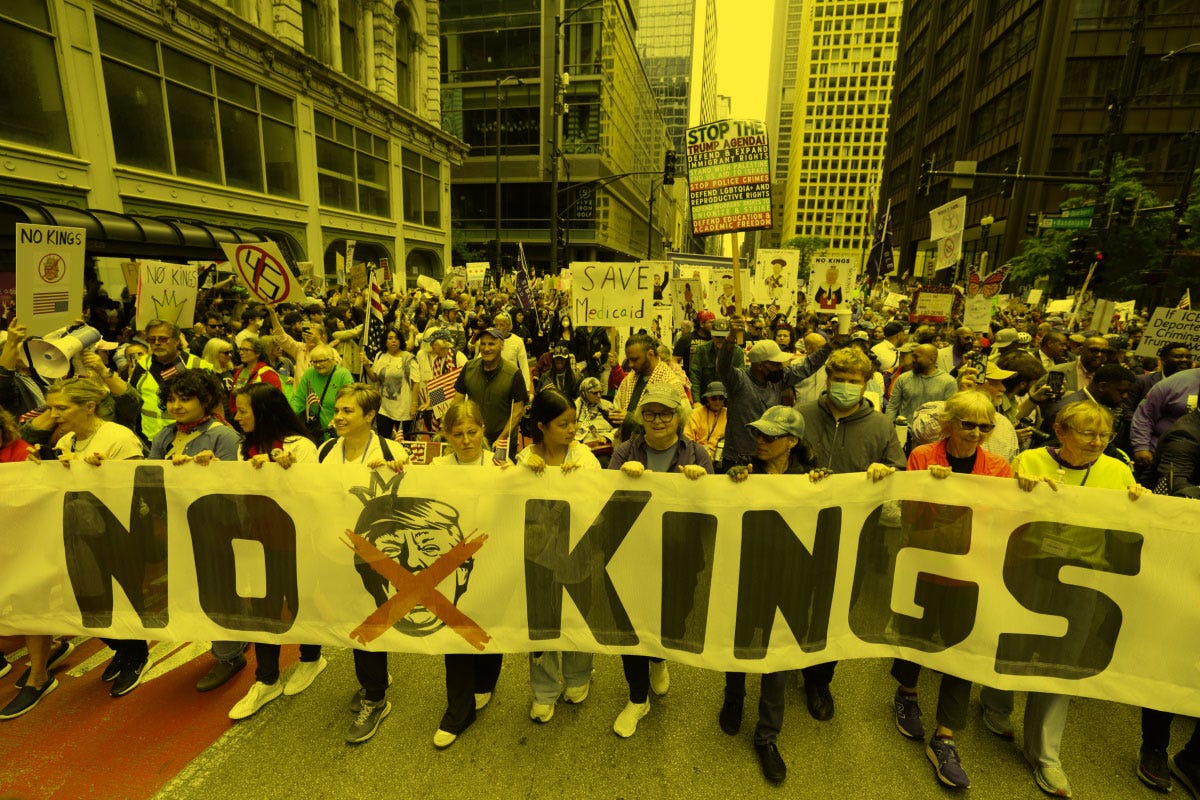 Protestors carry a banner that reads “No Kings” and features an image of Trump wearing a crown with an X covering his face. Protestors carry a banner that reads “No Kings” and features an image of Trump wearing a crown with an X covering his face.