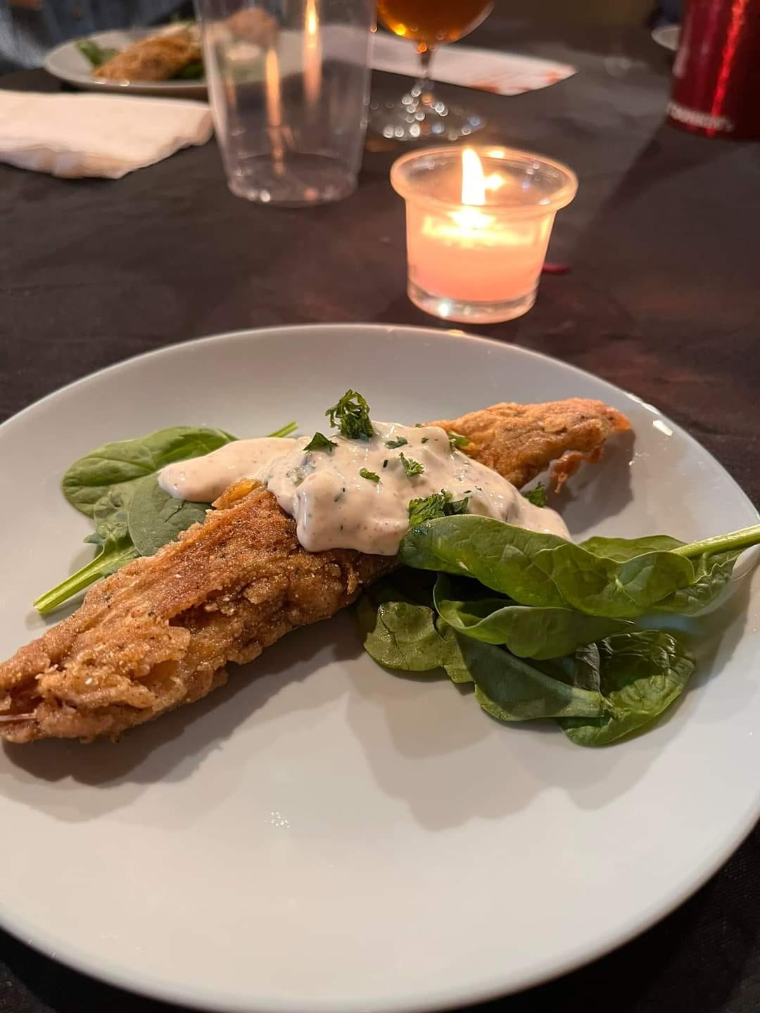 A plant-based dish resembling crispy fried fish alongside a serving of fresh spinach.
