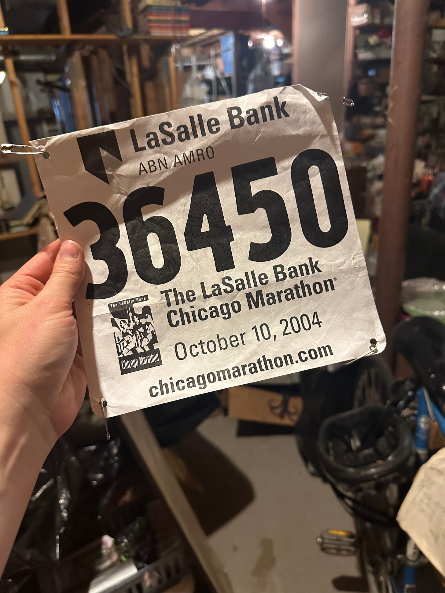 A close-up photo of a hand holding a marathon bib from the October 10, 2004 LaSalle Bank Chicago Marathon. The bib features the race logo, date, and the runner's number: 36450. A close-up photo of a hand holding a marathon bib from the October 10, 2004 LaSalle Bank Chicago Marathon. The bib features the race logo, date, and the runner's number: 36450.