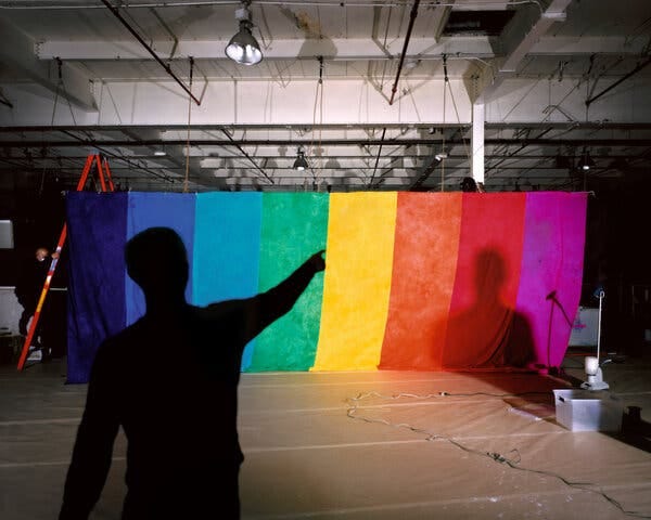 The silhouette of a person pointing falls on a large rainbow colored artwork.