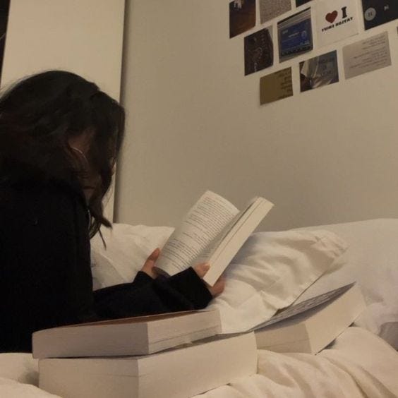 This may contain: a woman reading a book on top of a bed in a room with white sheets