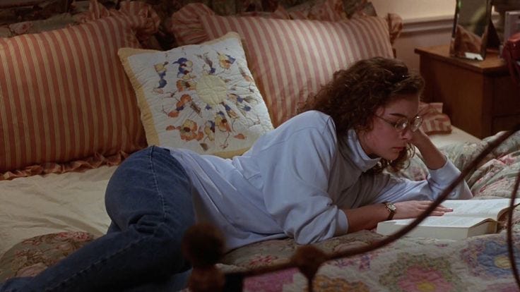 This may contain: a woman laying on top of a bed next to a lamp and pillow case in a bedroom